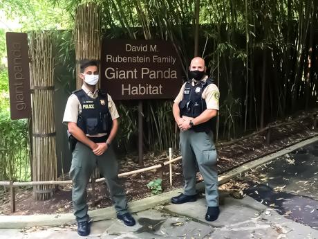 Two OPS Officers stand in front of the Giant Panda sign at the zoo while wearing uniform.