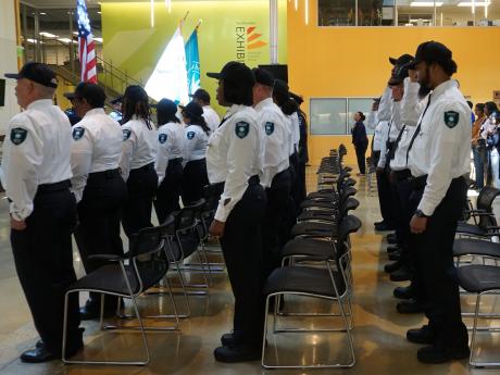 Four rows of OPS Officers wearing uniforms salute to the flag during their swearing in ceremony.