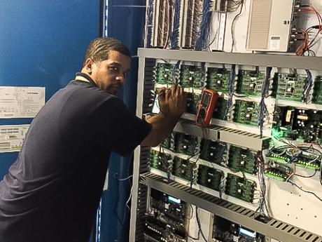 A man stands in front of alarm panel to make repairs. 